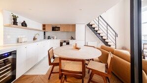 A modern kitchen with white cabinets, a dining area with a round table and chairs, and a staircase leading to an upper level. - Palais Royal Design - One Bedroom Apartment, Sleeps 5 (Paris)