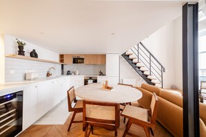 A modern kitchen with white cabinets, a dining area with a round table and chairs, and a staircase leading to an upper level. - Palais Royal Design - One Bedroom Apartment, Sleeps 5 (Paris)