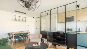 A modern living room with a dining area, a sofa, a coffee table, a TV, and a kitchen area with cabinets and a refrigerator. - Tour Eiffel Grenelle (Paris)