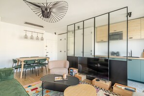 Ein modernes Wohnzimmer mit Essbereich, einer Couch, einem Couchtisch, einem Fernseher und einer Küchenzeile mit Schränken und einem Kühlschrank.