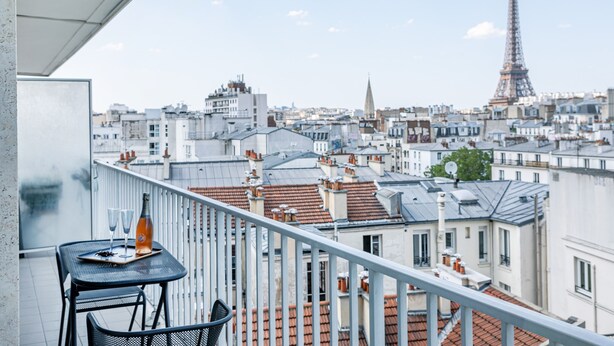 A balcony with a table, two chairs, and a bottle of wine, overlooking a cityscape with the Eiffel Tower in the distance. - Tour Eiffel Grenelle (Paris)