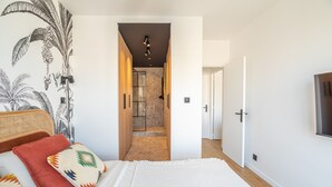A bedroom with a bed, pillows, a wall mural, a door, and a hallway leading to a bathroom. - Tour Eiffel Grenelle (Paris)