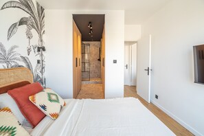 Ein Schlafzimmer mit Bett, Kissen, Wandgemälde, einer Tür und einem zur Toilette führenden Gang.