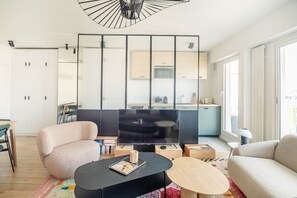 Ein modernes Wohnzimmer mit einer Couch, einem Couchtisch, einem Fernseher und einer Küche im Hintergrund.