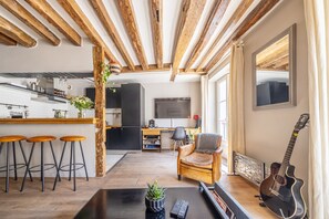 Une cuisine moderne avec des poutres en bois, un coin bar avec des tabourets, un espace détente avec un fauteuil en cuir et une guitare.