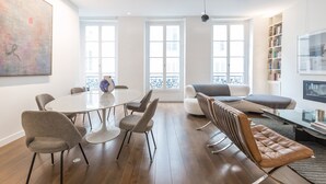 A modern living room with a dining table, chairs, a sofa, a coffee table, and a bookshelf. - Île Saint Louis Luxury (Paris)