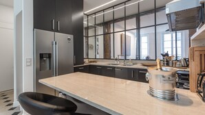 A modern kitchen with a large island, stainless steel appliances, and a Taittinger champagne bucket. - Île Saint Louis Luxury (Paris)