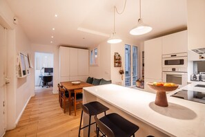 A modern kitchen with a central island, wooden dining table, and bar stools. - Republique Marais Charm (Paris)