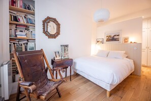 A bedroom with a bed, a wooden chair, a bookshelf, and a wall-mounted mirror. - Republique Marais Charm (Paris)