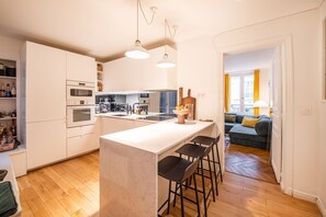 A modern kitchen with a central island, bar stools, and a dining area. - Republique Marais Charm (Paris)