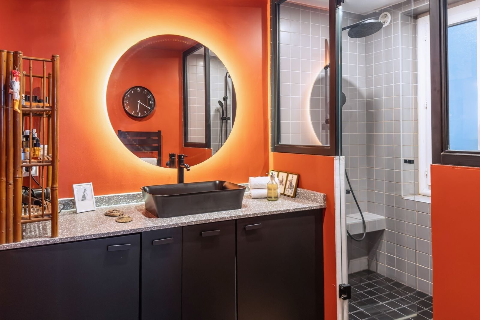 A modern bathroom with a round mirror, a black sink, and a shower area.