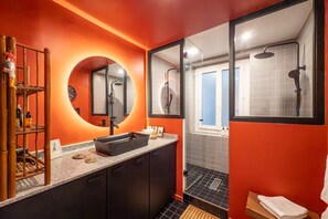 A modern bathroom with a black sink, a round mirror, and a shower area. - Republique Marais Charm (Paris)