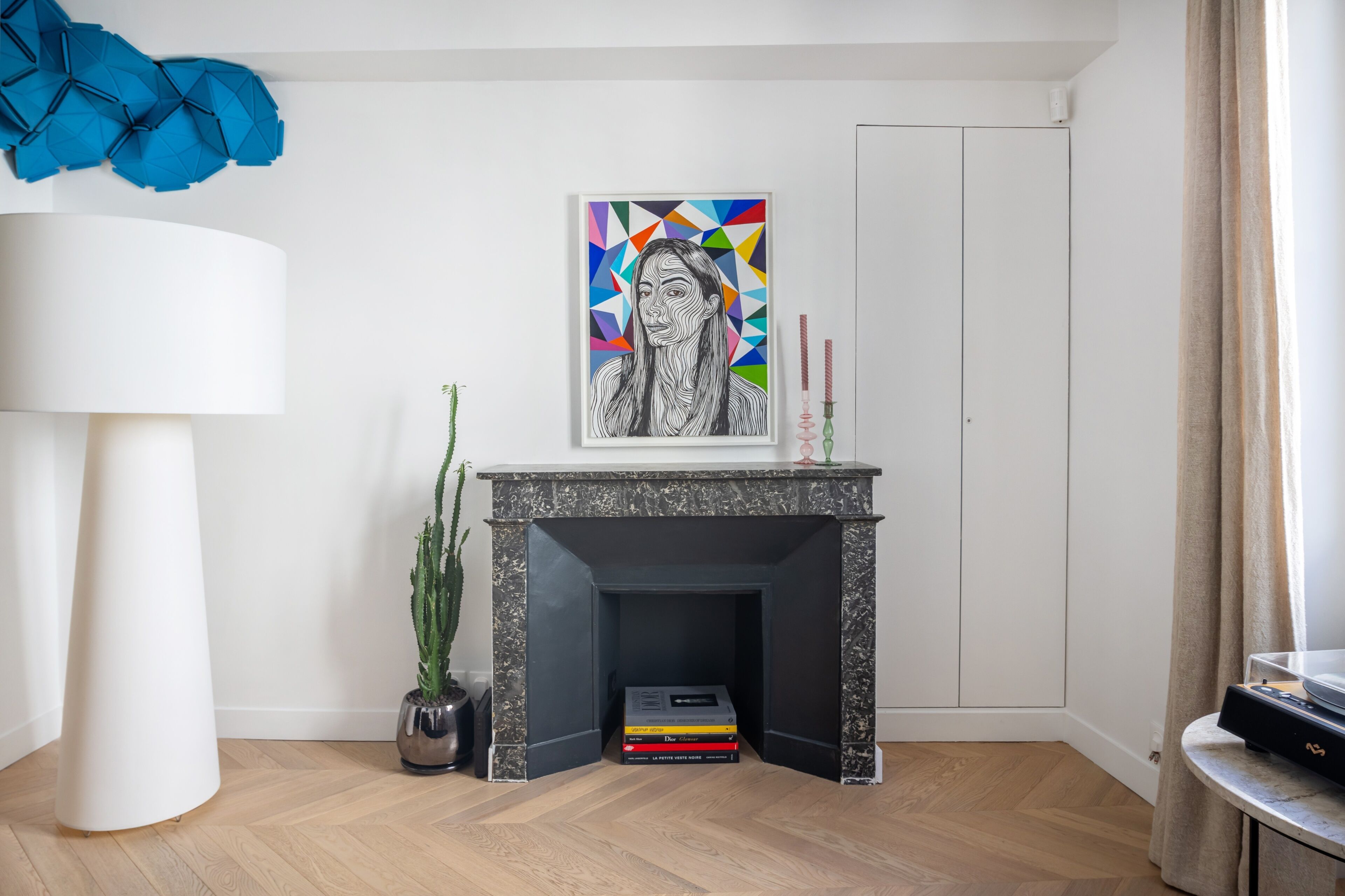 A modern living room with a fireplace, a framed artwork, a potted plant, and a stack of books.