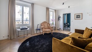 A living room with a black rug, a patterned armchair, a brown sofa, and a small table with a plant. - Opéra Style - One Bedroom Apartment, Sleeps 2 (Paris)