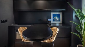 A modern kitchen with dark cabinetry, a black dining table, and wicker chairs. - Opéra Style - One Bedroom Apartment, Sleeps 2 (Paris)