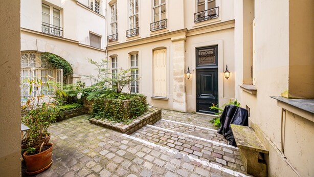 A courtyard with a brick pathway, potted plants, and a black door. - Quartier Latin Loft Maubert (Paris)