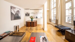 A modern living room with a dining area, a kitchen in the background, and large windows. - Quartier Latin Loft Maubert (Paris)