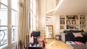 A modern living room with a spiral staircase, a bookshelf, a sofa, and a table. - Quartier Latin Loft Maubert (Paris)