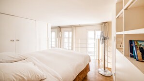 A bedroom with a large bed, a floor lamp, a bookshelf, and a window with curtains. - Quartier Latin Loft Maubert (Paris)