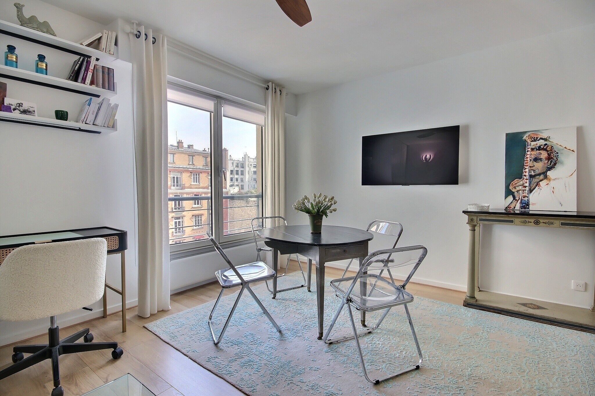A modern living room with a dining table, chairs, a bookshelf, a TV, and a painting.