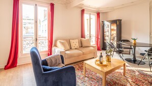 Ein Wohnzimmer mit einer Couch, einem blauen Sessel, einem Couchtisch und einem Essbereich mit Tisch und Stühlen.