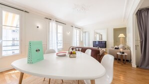 A modern living room with a dining area, a sofa, a TV, and a lamp. - Marais Saint Paul - Two Bedroom Apartment, Sleeps 6 (Paris)