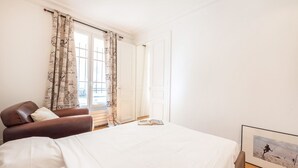 A bedroom with a bed, a chair, a window with curtains, and a framed picture on the wall. - Marais Saint Paul - Two Bedroom Apartment, Sleeps 6 (Paris)