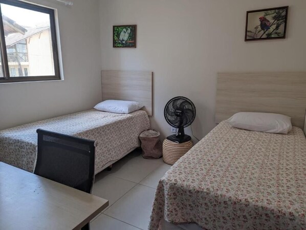 A room with two single beds, a desk, a chair, a standing fan, and a window. - Sonhos da Serra (Bananeiras)