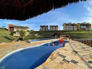 A swimming pool with a slide, surrounded by a stone deck, with buildings in the background. - Sonhos da Serra (Bananeiras)
