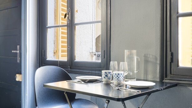 Ruokapöytä tuoleineen, kannu, kupit ja lautaset.