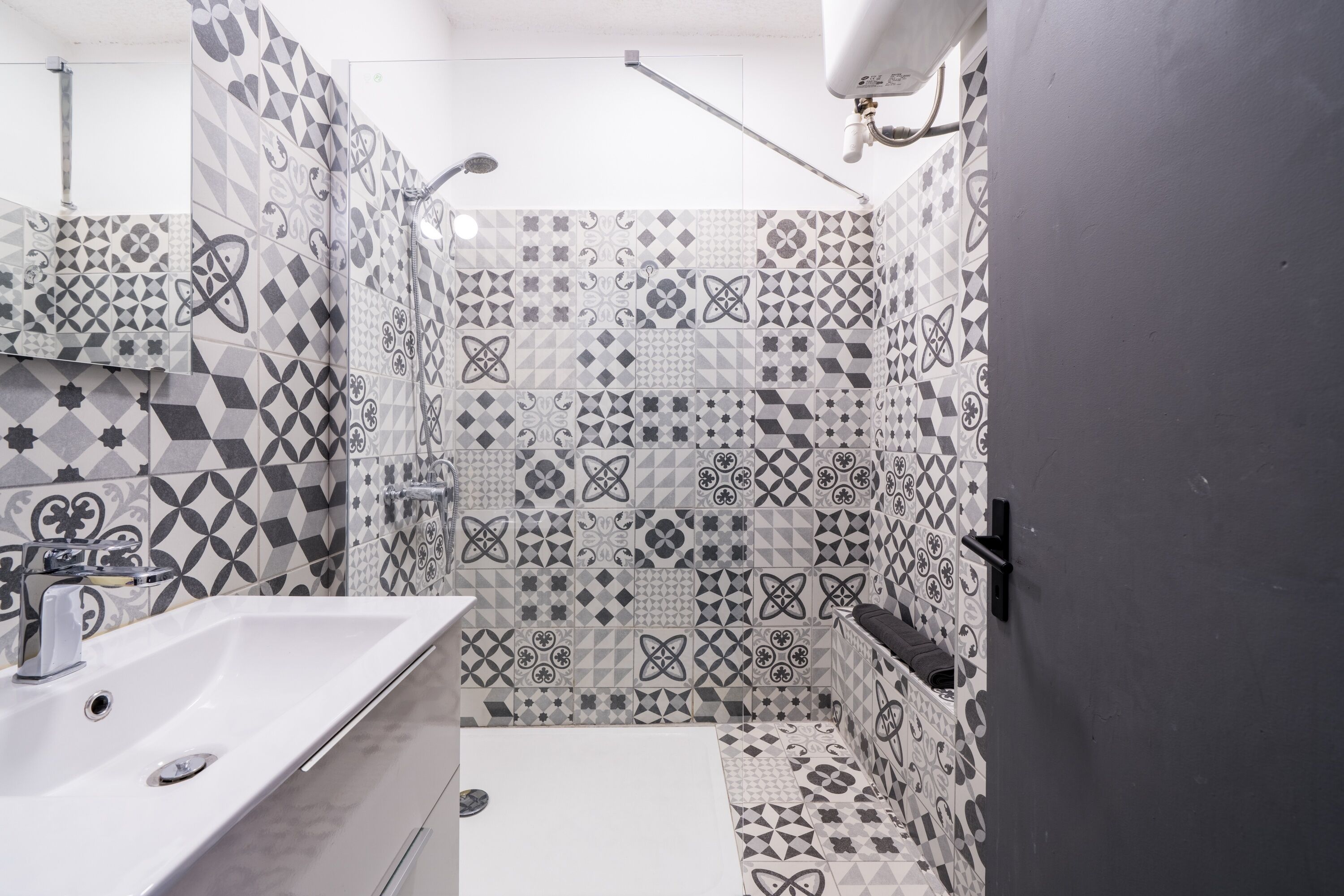 A bathroom with a white sink, a shower, and patterned tiles on the walls.