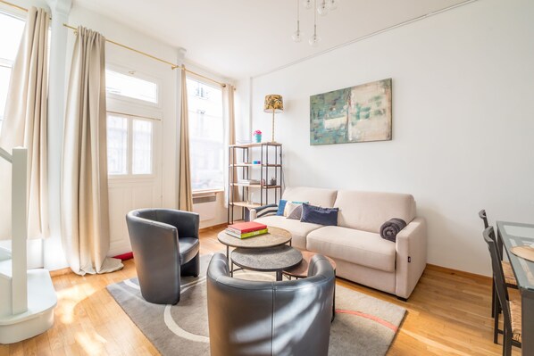 Ein modernes Wohnzimmer mit einer Couch, zwei Sesseln, einem Couchtisch, einem Bücherregal und einem Bild an der Wand.