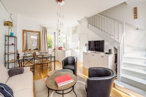 Ein modernes Wohnzimmer mit einer Couch, Sesseln, einem Esstisch, einem Fernseher und einer Treppe.