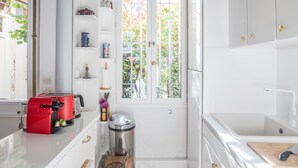 A modern kitchen with white cabinetry, a red toaster, a trash bin, and a window with a view of greenery. - Bon Marché Sevres - Two Bedroom Apartment, Sleeps 4 (Paris)