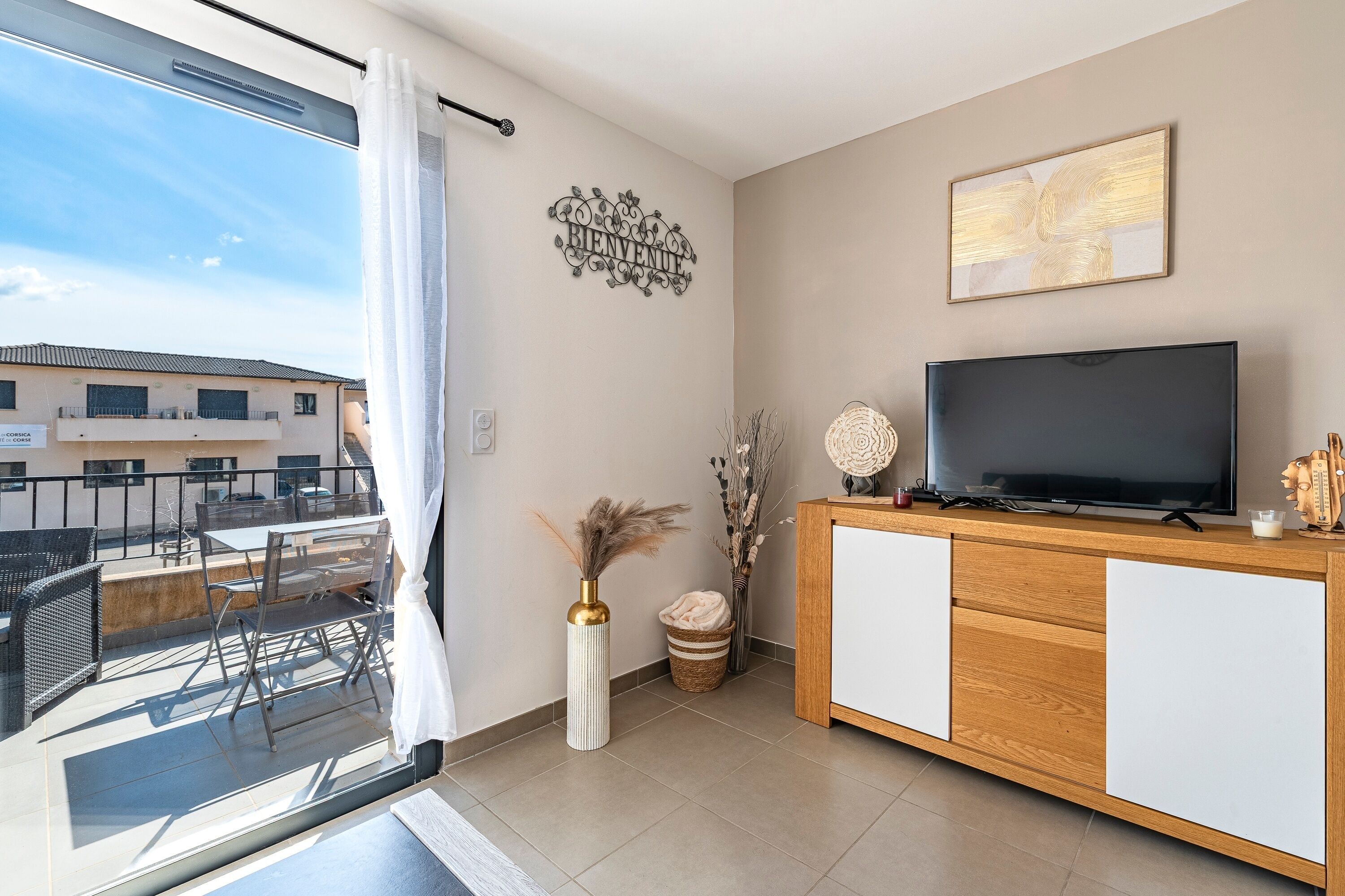 A modern living room with a TV, wooden cabinet, and a balcony with outdoor furniture.