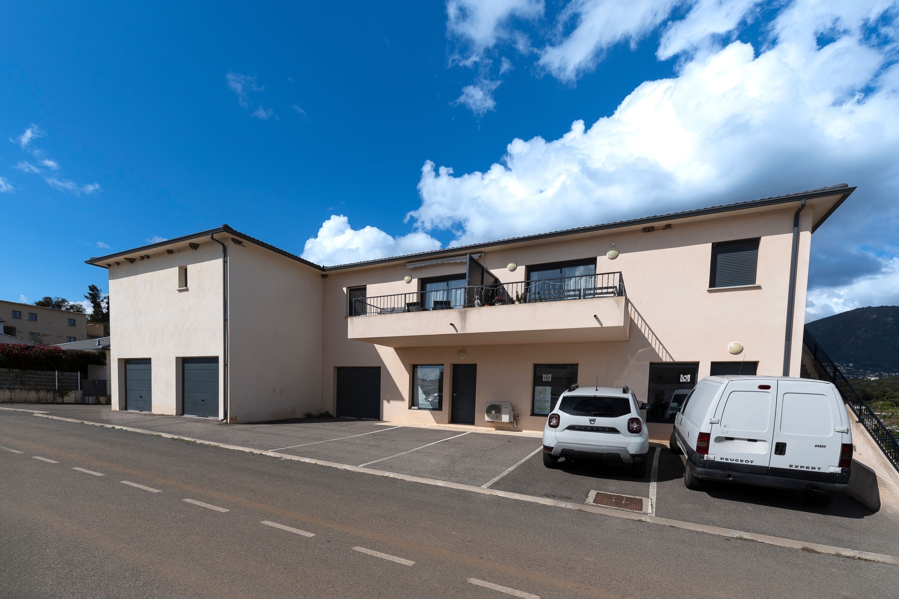 A two-story building with a parking area, a white van, and a white car.