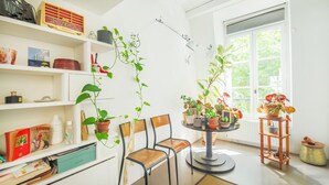 Una stanza con una libreria, due poltrone, un tavolino rotondo con piante in vaso e una finestra vista verde.