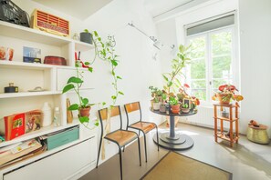 A room with a bookshelf, two chairs, a round table with potted plants, and a window with a view of greenery. - Batignolles Home - Three Bedroom Apartment, Sleeps 8 (Paris)