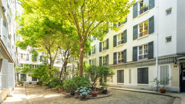 Un cortile lastricato con piante in vaso, un albero e edifici a più piani con balconi.