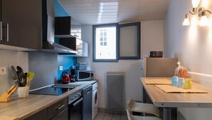 Cocina compacta con lavadora, microondas y un pequeño comedor con mesa y sillas.