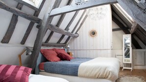 Un dormitorio con techo inclinado, cama con ropa de cama estampada, un espejo y un mueble blanco pequeño.