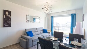 Ein modernes Wohnzimmer mit einem grauen Sofa, blauen Kissen, einem Glastisch und einem Essbereich mit Stühlen und einer Lampe.