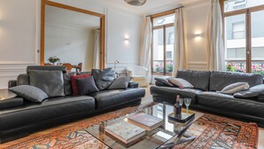 A modern living room with two black leather sofas, a glass coffee table, and a patterned rug. - Jardin du Luxembourg Home (Paris)