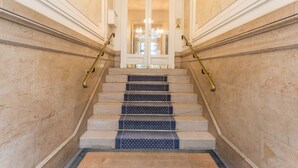 A grand staircase with marble walls, a handrail, and a carpeted landing. - Jardin du Luxembourg Home (Paris)