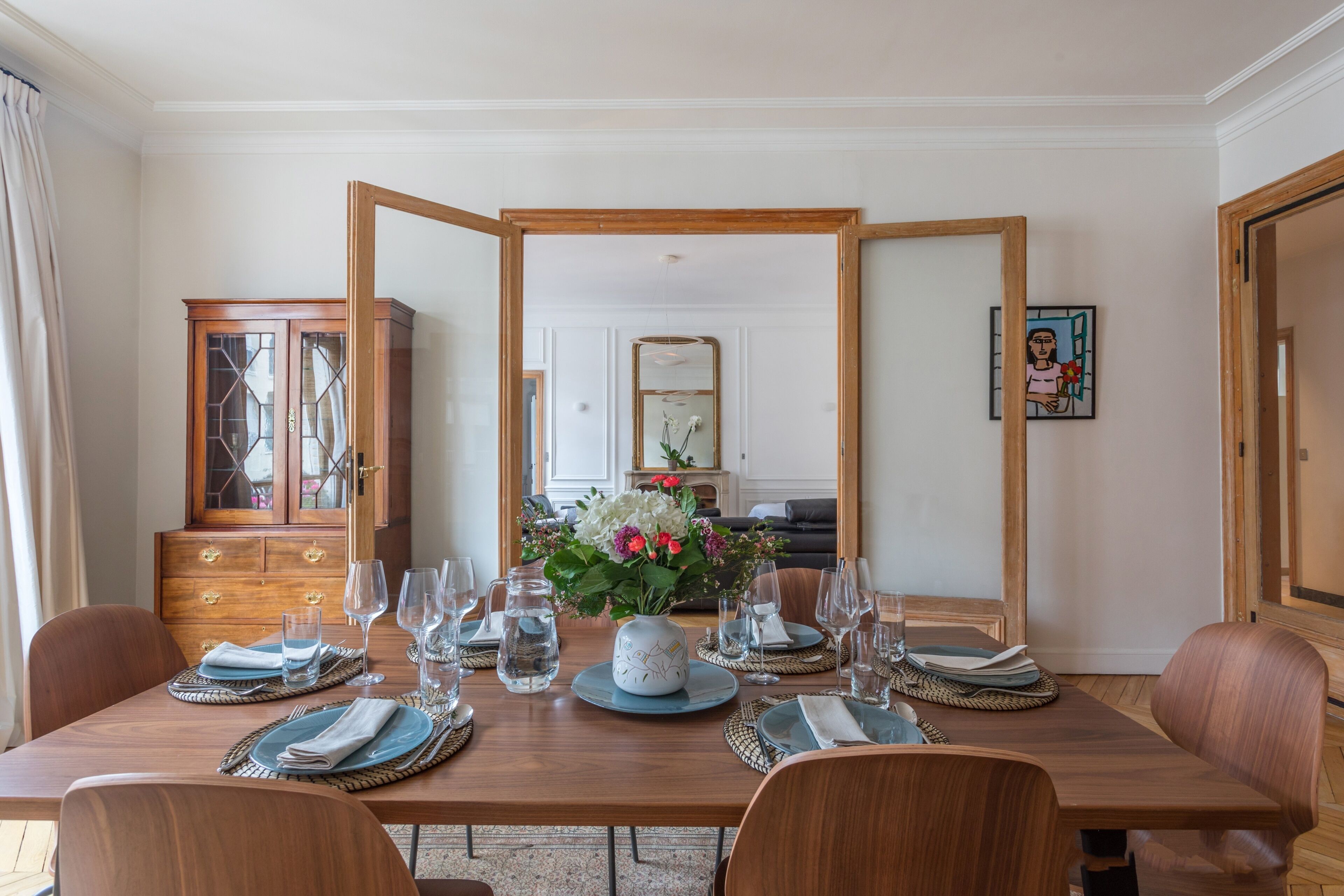 A dining room with a wooden table set for four, a cabinet, and a mirror.