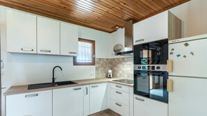 Uma cozinha moderna com armários brancos, teto de madeira, forno embutido e geladeira.