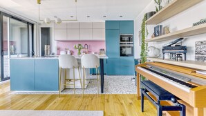A modern kitchen with a central island, bar stools, a piano, and a dining area with a pink wall. - L'Atelier de Sèvres - 2 places de parking (Boulogne-Billancourt)