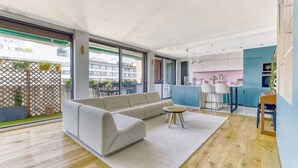 A modern living room with a sofa, a round table, and a view of a kitchen and balcony. - L'Atelier de Sèvres - 2 places de parking (Boulogne-Billancourt)