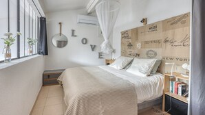 Un dormitorio con cama, mesita de noche, estanterías, ventana con cortinas y pared decorada con letras.