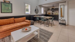 Una sala de estar moderna con un sofá, una mesa de comedor y sillas. Hay una zona de cocina con armarios y electrodomésticos.